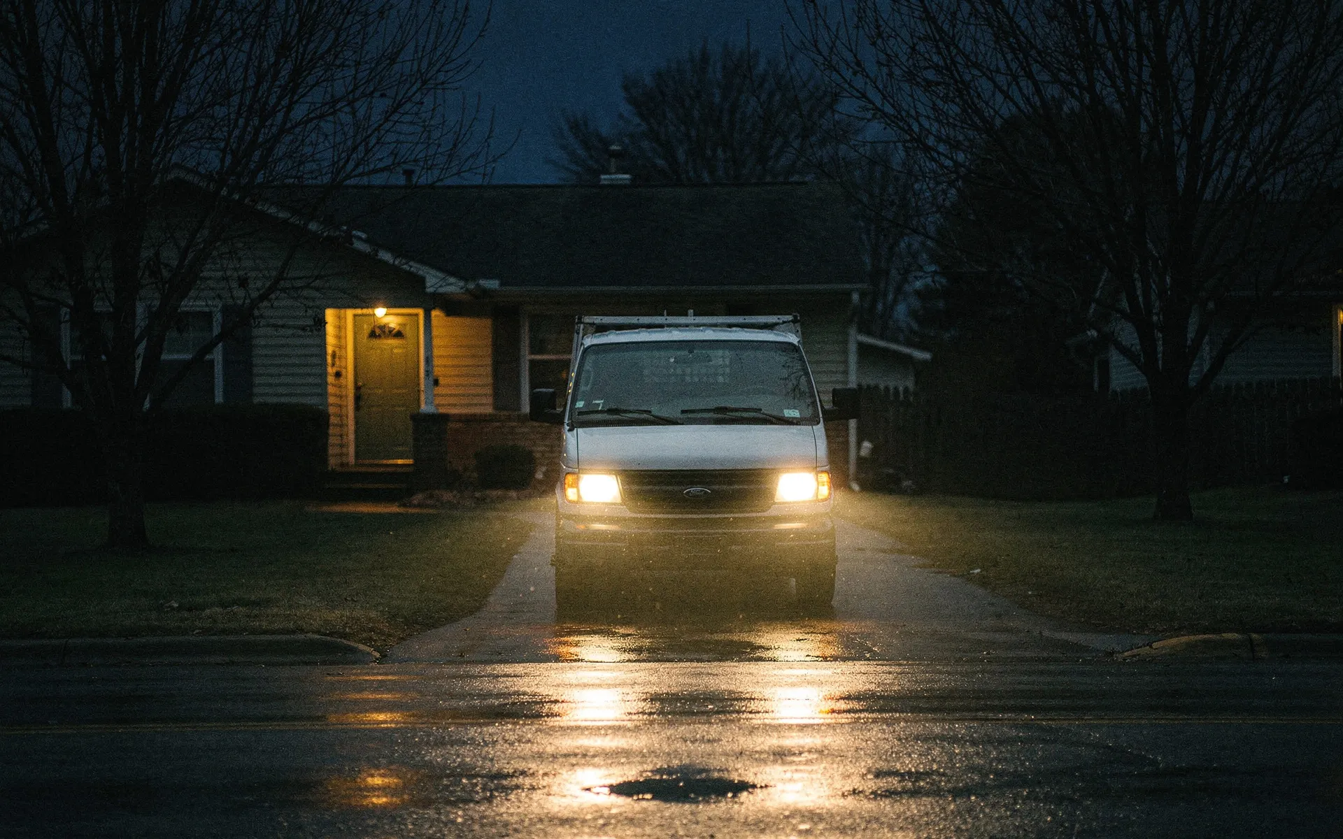 A service van in a Lexington driveway at night, headlights on, porch light behind.