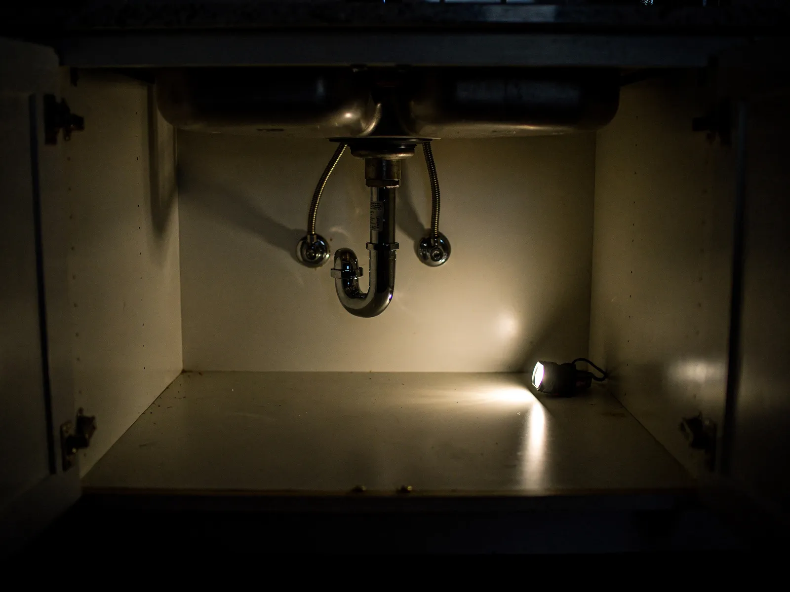 Under a kitchen sink at night, lit by a work light.